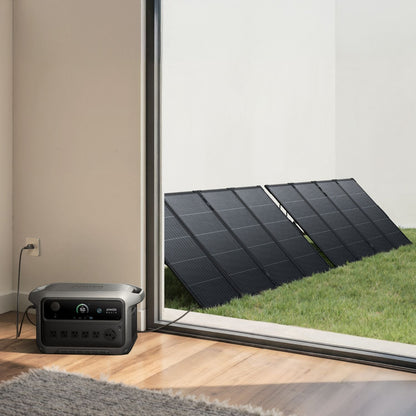 Anker SOLIX C2000 Gen 2 Portable Power Station next to a window with solar panels on a grassy area outside.