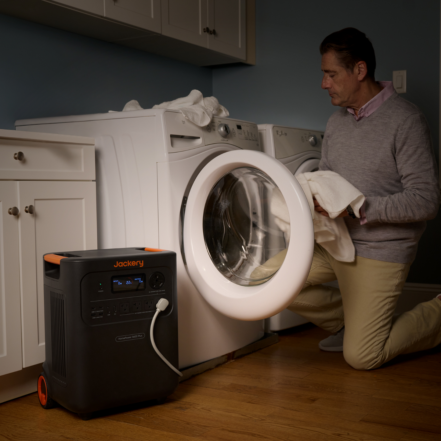 Man using a JJackery HomePower 3600 Plus Portable Power Station next to a washing machine in a laundry room.